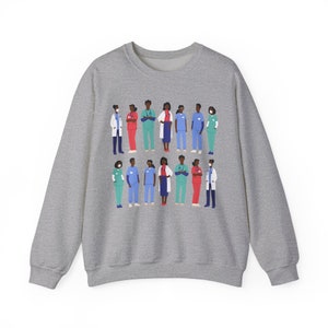 May include: A gray sweatshirt with a graphic print of a group of diverse healthcare workers wearing scrubs and masks. The workers are standing in a line, and the graphic is centered on the sweatshirt.