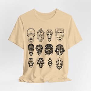 May include: A beige t-shirt with a black and white print of 12 African tribal masks. The masks are arranged in four rows of three masks each.