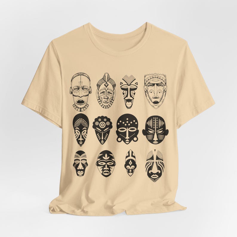 May include: A beige t-shirt with a black and white print of 12 African tribal masks. The masks are arranged in four rows of three masks each.