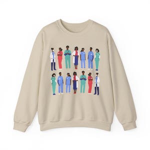May include: A beige sweatshirt with a graphic print of a diverse group of healthcare workers wearing scrubs, masks, and lab coats. The workers are standing in a line, and some are holding medical equipment.
