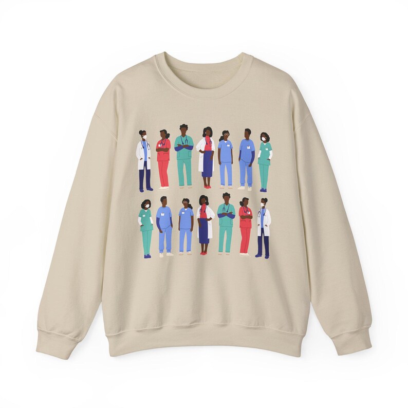 May include: A beige sweatshirt with a graphic print of a diverse group of healthcare workers wearing scrubs, masks, and lab coats. The workers are standing in a line, and some are holding medical equipment.