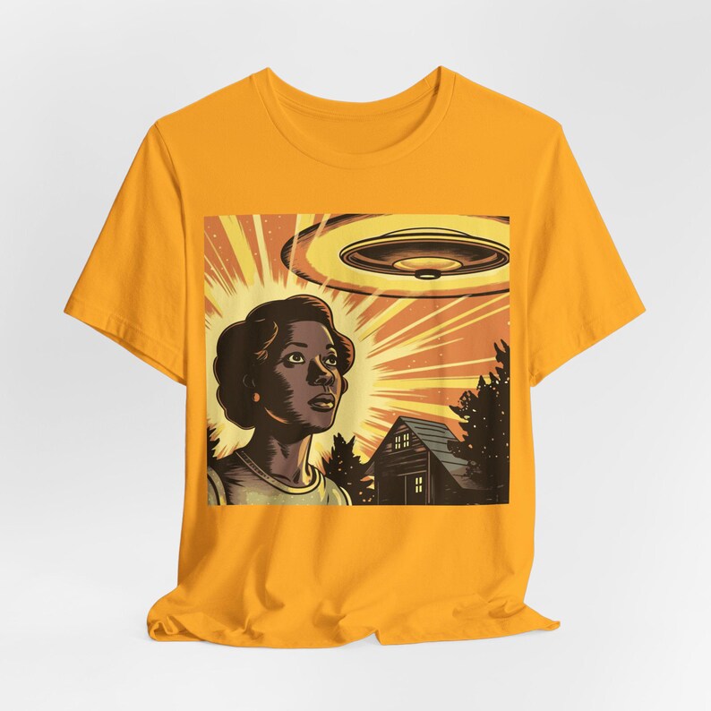 May include: A yellow t-shirt with a graphic print of a woman looking up at a flying saucer. The graphic also includes a house and trees in the background.