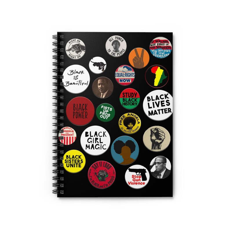 May include: A black spiral notebook with colorful button pins featuring various slogans and images related to Black history and culture. The pins include phrases like "Black Power", "Black is Beautiful", "Black Lives Matter", and "Study Black History".
