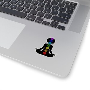 May include: A black silhouette of a person meditating with seven colorful chakras, representing the seven energy centers of the body, on a white background.