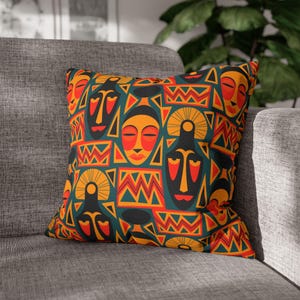 May include: A square throw pillow featuring a repeating pattern of stylized faces and geometric shapes in shades of orange, red, yellow, and dark teal. The design includes abstract masks with almond-shaped eyes and zigzag line motifs.