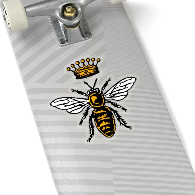 Puede incluir: Una abeja negra y amarilla con alas blancas y una corona dorada encima. La abeja est&aacute; sobre un fondo rayado gris y blanco.