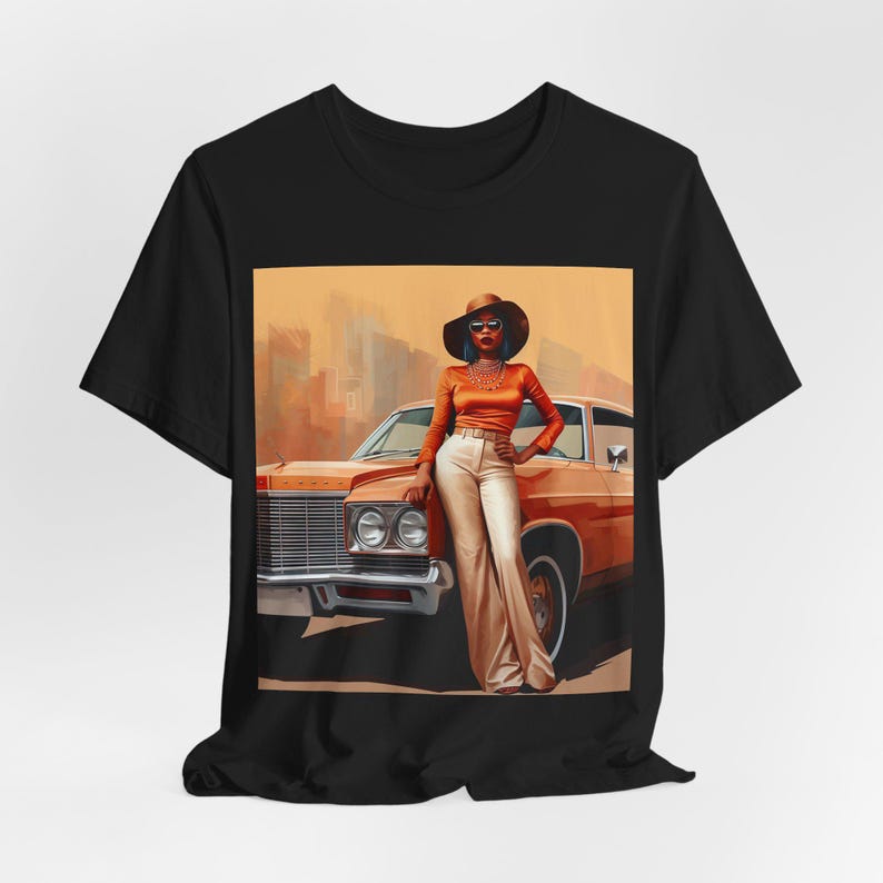 Op de afbeelding: Een zwart T-shirt met een grafische print van een vrouw in een bruine hoed en een oranje outfit, die naast een oranje oldtimer staat.