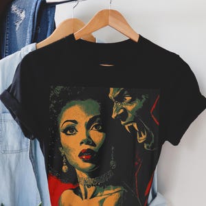 Könnte beinhalten: Schwarzes T-Shirt mit einem Grafikdesign im Vintage-Stil, das eine Frau und ein Monster zeigt. Die Frau hat rote Lippen und ein Halsband. Das Monster hat grüne Haut und Fangzähne.