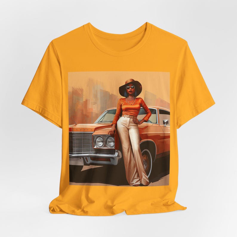 Op de afbeelding: Een geel T-shirt met een grafische print van een vrouw in een bruine hoed en zonnebril die naast een vintage auto staat. De vrouw draagt een bruin topje, een witte broek en een ketting. De auto is bruin en heeft een wit interieur.