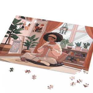 May include: A jigsaw puzzle featuring an illustration of a person knitting in a cozy room. The person is wearing a pink sweater and headband, surrounded by plants and artwork. The color palette is warm, with shades of pink, brown, and green.