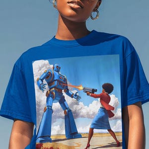 May include: Bright blue t-shirt with a striking image of a vintage robot and a woman in a red jacket and blue skirt, aiming a gun. The artwork is set against a blue sky with clouds, creating a dynamic and eye-catching design.
