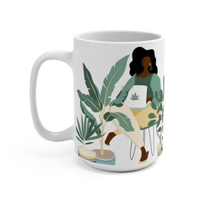 May include: White ceramic mug with a colorful illustration of a person sitting in a chair surrounded by plants. The person is wearing a green shirt and has long black hair. The plants are green and yellow.