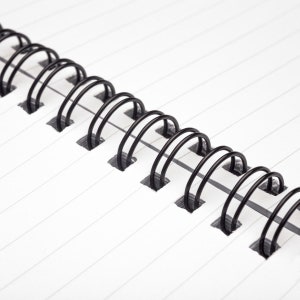 May include: Close-up of a black wire binding on a white lined notebook.