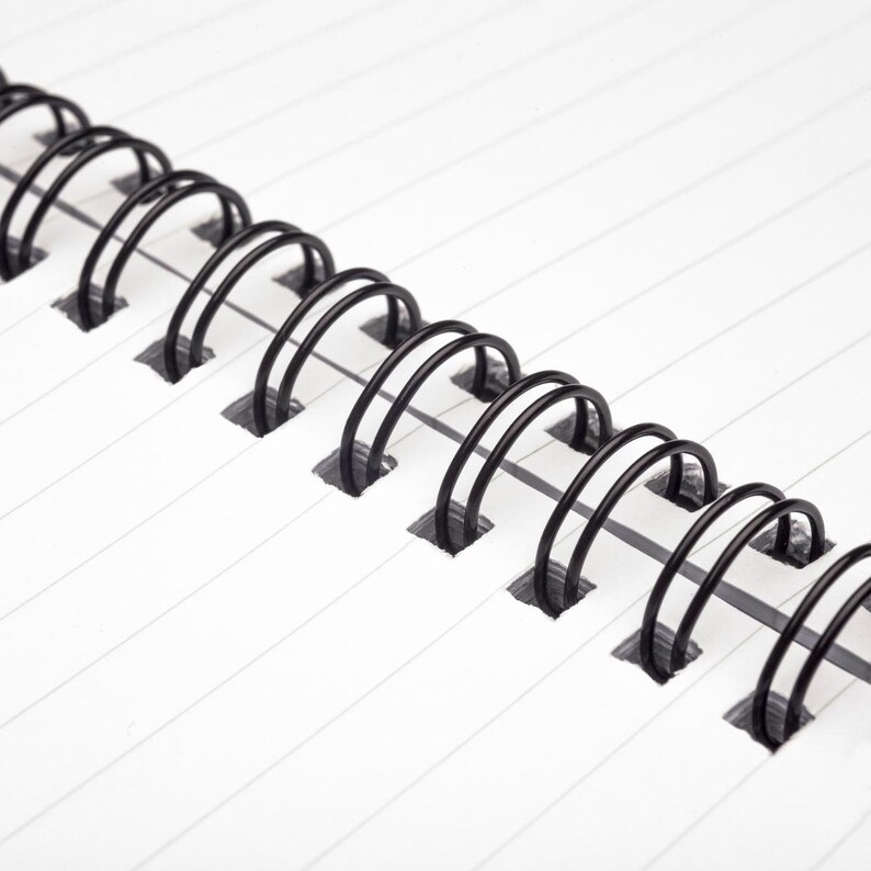 May include: Close-up of a black wire binding on a white lined notebook.