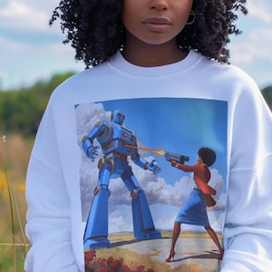 May include: White sweatshirt featuring a vibrant graphic of a blue robot facing a person in a red jacket and blue skirt, holding a gun. The artwork is set against a blue sky with clouds and a landscape background.