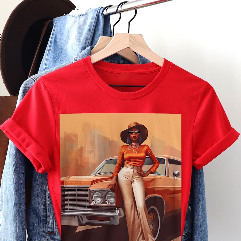 Op de afbeelding: Rood T-shirt met een grafische print van een vrouw met een bruine hoed en zonnebril, die naast een oldtimer staat. De auto is bruin en heeft een wit interieur.