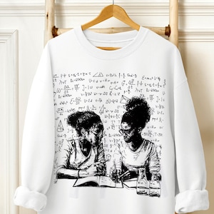 以下が含まれることがあります： 黒と白のイラストが描かれた白いスウェットシャツ。イラストは、本と鉛筆を使って勉強している2人の人物を描いています。イラストは手書きの数学の式で囲まれています。