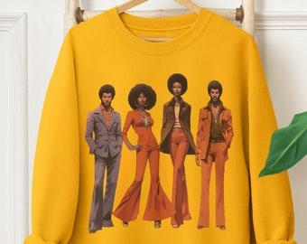 May include: Mustard yellow sweatshirt featuring a retro illustration of four people in 1970s attire. The figures are depicted in various outfits, including bell-bottom pants and suits, in shades of orange, brown, and gray.