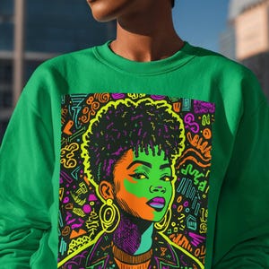 Könnte beinhalten: Grünes Sweatshirt mit einem lebendigen Grafikporträt einer Frau in Neonfarben. Das Kunstwerk zeigt eine schwarze Jacke, lila Ohrringe und eine neongelbe Afro-Frisur. Das Design ist von abstrakten Formen und Linien umgeben.