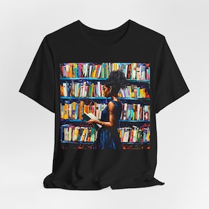 Może przedstawiać: Czarny T-shirt z kolorową grafiką osoby stojącej przed regałem wypełnionym książkami. Osoba trzyma książkę w ręku.