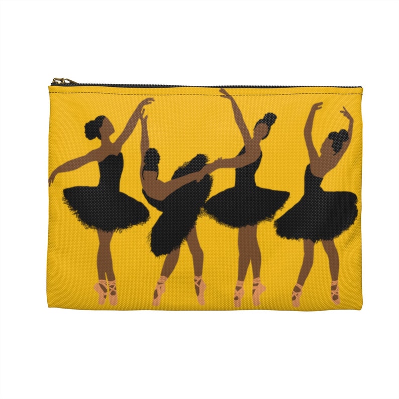 Pode incluir: Uma bolsa amarela com z&iacute;per com um gr&aacute;fico de quatro bailarinas em tutus pretos e sapatilhas de ponta. As bailarinas est&atilde;o em v&aacute;rias poses de dan&ccedil;a em um fundo amarelo. O z&iacute;per &eacute; dourado.