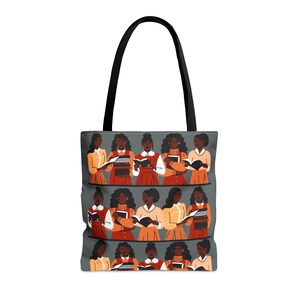 Puede incluir: Bolso tote gris con asas negras. Presenta una ilustraci&oacute;n repetida de mujeres leyendo libros. Las mujeres visten varios atuendos con tonos naranja, rojo y amarillo. Ideal para llevar libros y otros art&iacute;culos.