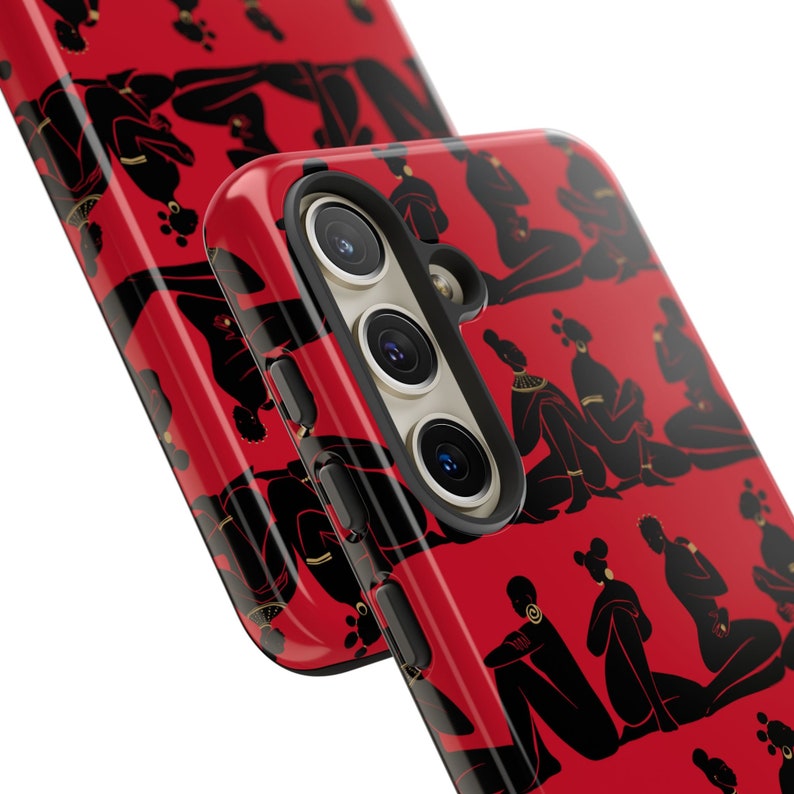 Puede incluir: Una funda de tel&eacute;fono roja con un patr&oacute;n negro y dorado de figuras estilizadas. La funda tiene un recorte para una c&aacute;mara de triple lente.
