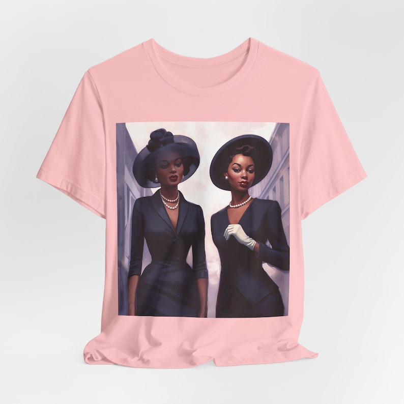 May include: A pink t-shirt featuring a graphic print of two women in black dresses and hats. The women are standing next to each other and looking at the camera.