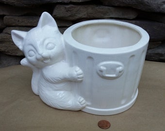 May include: White ceramic planter shaped like a cat holding a white ceramic bin. The bin has a lid and a handle.