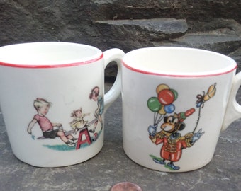May include: Two white ceramic mugs with red trim. One mug features a cartoon illustration of children on a seesaw. The other mug features a cartoon illustration of a clown with balloons.