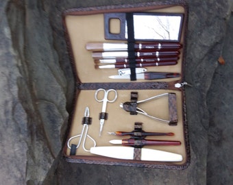 May include: A brown leather travel case with a zipper closure, containing a set of manicure tools. The tools include nail clippers, tweezers, a nail file, a cuticle pusher, and a small mirror.