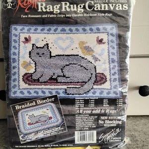 May include: A rug hooking kit featuring a colonial cat design. The kit includes a printed canvas, needle, and instructions. The canvas is 18 inches by 24 inches. The kit also includes a braided border pattern. The kit is from the Rugpoint brand.