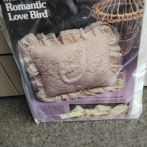 May include: A pillow kit by Yours Truly, called "Romantic Love Bird". The kit includes a pink pillow with an embroidered design of a bird in a cage. The pillow is 16 inches by 20 inches, including the ruffle.