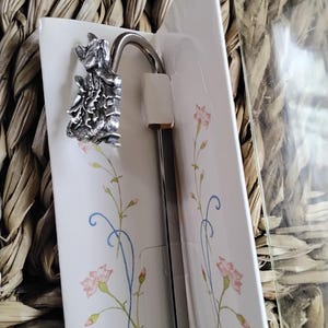 May include: A silver bookmark featuring a detailed design of two rabbits perched on a branch. The bookmark is displayed against a white background with a floral pattern.