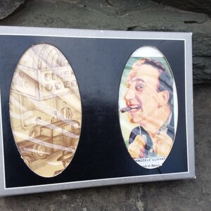 May include: A vintage-style set of two coasters featuring a black and white illustration of a man smoking a cigar and a black and white illustration of a car driving past a building with the text "Cinema Odeon".