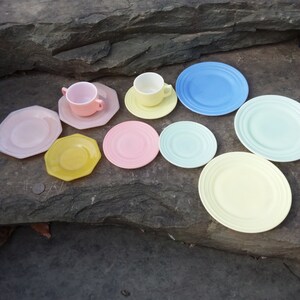 May include: A set of pastel-colored teacups and saucers, including a light blue saucer, a light green saucer, a yellow saucer, a pink saucer, a light yellow saucer, and a pink saucer. The teacups are white with a pink rim.