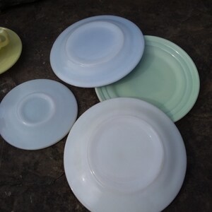 May include: Four vintage white milk glass plates in various shades of blue and green. The plates are stacked on top of each other.