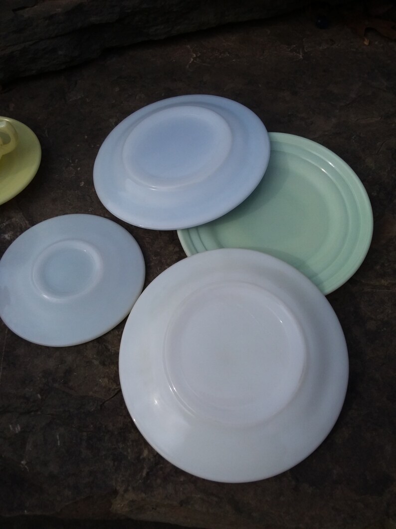 May include: Four vintage white milk glass plates in various shades of blue and green. The plates are stacked on top of each other.