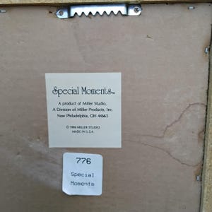 May include: The back of a framed artwork with a sawtooth hanger. A white label reads "Special Moments" and details the manufacturer, Miller Studio, and its location in New Philadelphia, Ohio. A smaller label displays the number "776" and the words "Special Moments."
