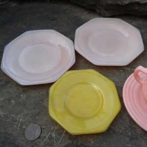 May include: Four octagonal shaped plates, two pink and two yellow, with a smaller plate in the center of each. The plates are on a gray textured surface.