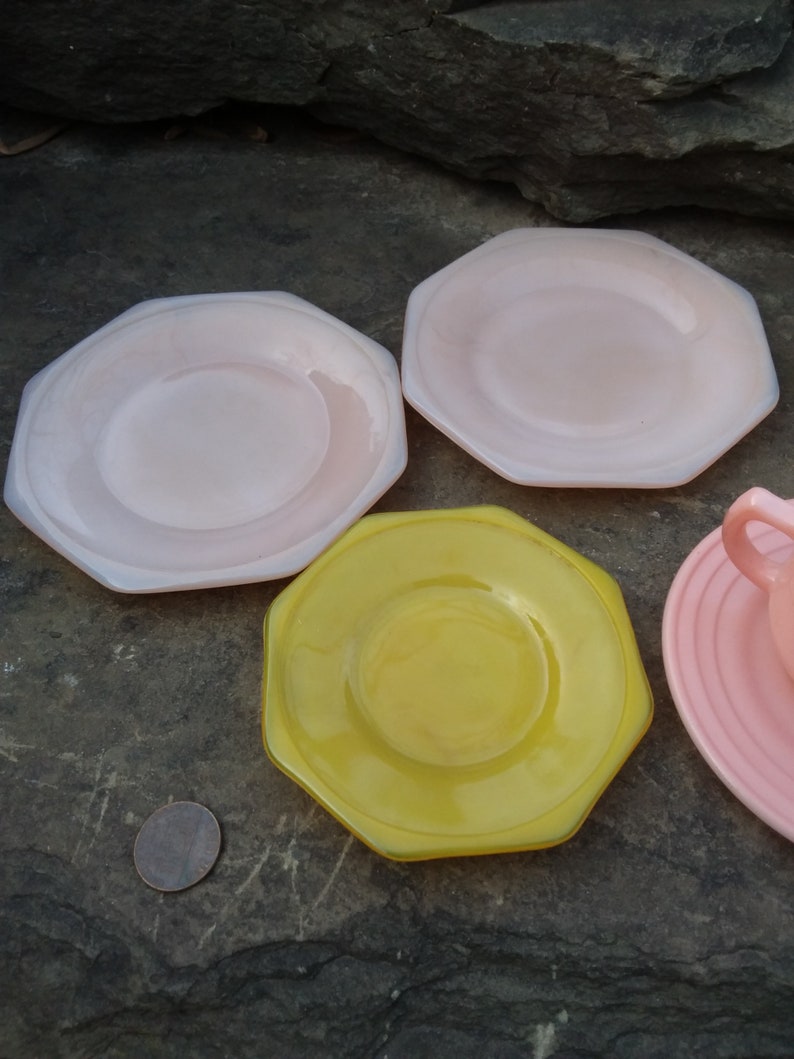 May include: Four octagonal shaped plates, two pink and two yellow, with a smaller plate in the center of each. The plates are on a gray textured surface.