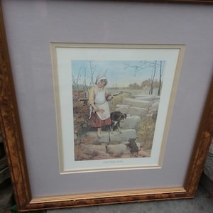 May include: A framed print of a painting depicting a young girl in a white dress and a red hat walking down a stone path with two dogs. The painting is titled "The First Step".