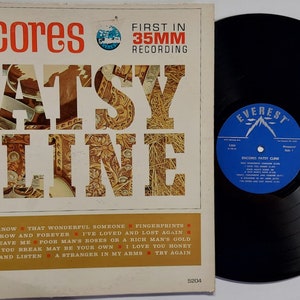 May include: Vintage vinyl record album cover for Patsy Cline's "Encores." The album cover features the artist's name in large, ornate letters with a floral pattern. The record itself is black, with a blue and white label. The album title and song titles are also visible.