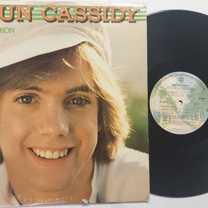 May include: A vinyl record album cover featuring a portrait of Shaun Cassidy, a young man with brown hair wearing a white hat. The album title is "Da Doo Ron Ron" and the text "Corban the hit single" is also visible. The album cover is a light yellow color with green stripes.