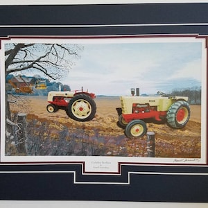 May include: Framed print of two vintage tractors in a field. The tractors are cream and red, with large wheels. The print is matted and framed in a dark blue frame. The title "Cochran Brothers" is at the bottom.