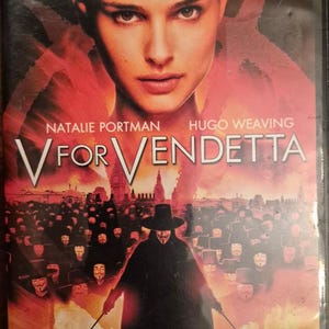 May include: A V for Vendetta DVD case featuring a widescreen edition label at the top. The cover displays a large portrait of Natalie Portman above a crowd of people wearing Guy Fawkes masks, with the title V for Vendetta and Hugo Weaving listed.