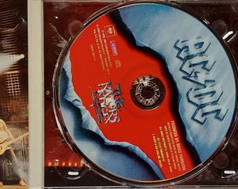 May include: An AC/DC The Razors Edge music CD in a plastic case. The cover features a blue background with a torn center revealing a red surface and the band name and album title in silver lettering. The disc itself is red with a blue torn edge.