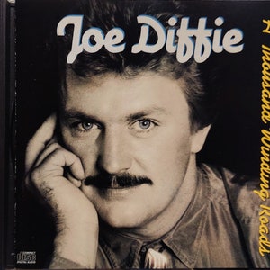May include: A black and white photo of Joe Diffie on a CD cover. The title of the album is "A Thousand Winding Roads".