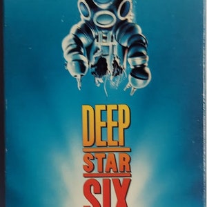 May include: VHS tape for the movie "Deep Star Six". The cover features a diver in a vintage diving suit against a blue underwater backdrop. The title is in orange and red block letters. The tagline reads "Not All Aliens Come From Space. Save Your Last Breath... To Scream."