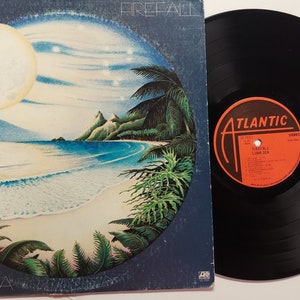 May include: A vinyl record album cover with a blue background and a circular image of a tropical beach scene with a full moon, palm trees, and a sandy beach. The album title is "Luna Sea" and the band name is "Firefall". The record label is "Atlantic".